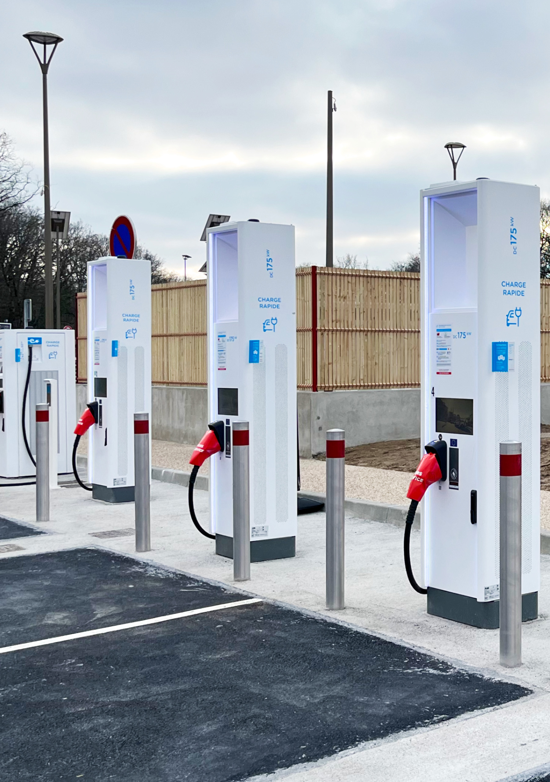 A modern electric vehicle charging station with dual charging cables and a digital payment interface in a commercial parking lot.