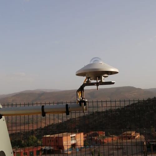 Close-up of a three-cup anemometer meteorological tool spinning to measure wind speed against a clear blue sky.